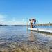 Man and dog on a dock by a lake with clear water and blue sky.