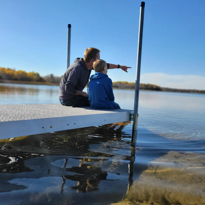 Man and child sitting on a dock by a lake, pointing at something in the water.