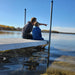 Man and child sitting on a dock by a lake, pointing at something in the water.