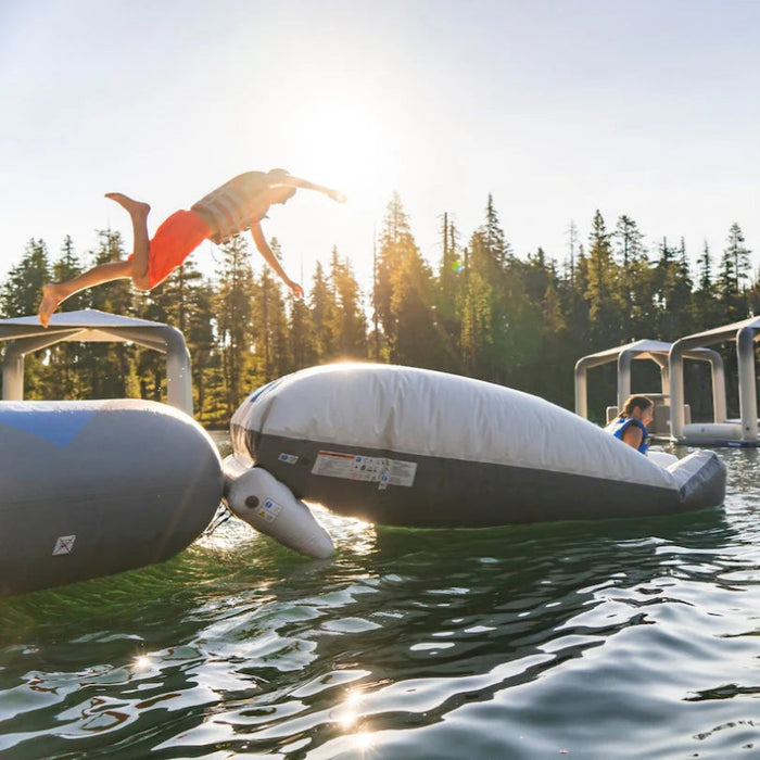 Person jumping off an inflatable structure into a body of water with trees in the background