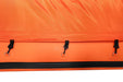 Close-up of an orange bag with black zippers and hooks on a white background