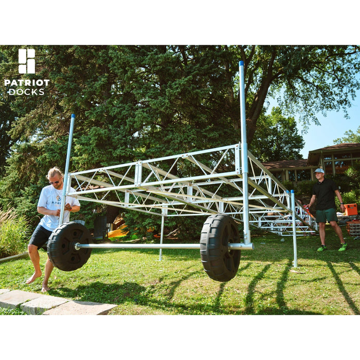 Two men working on a large metal frame with wheels outdoors, branded 'Patriot Docks'.